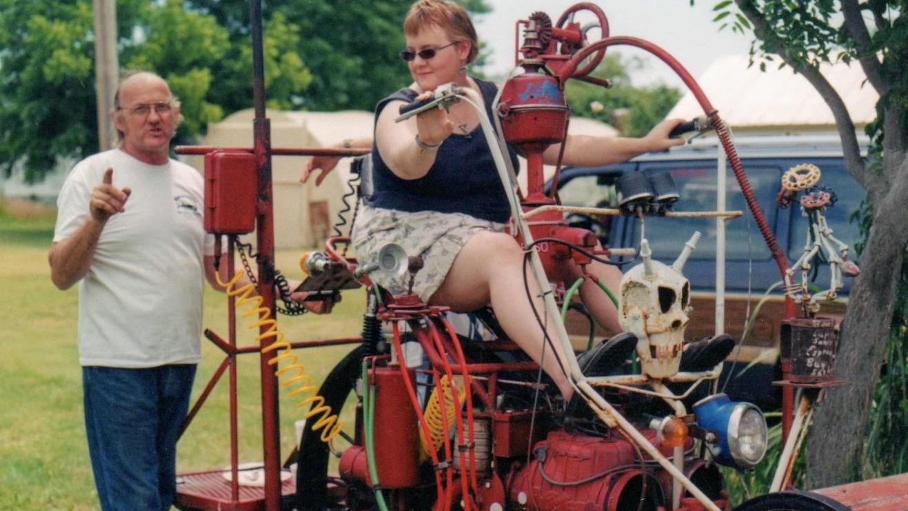 Image of Beverly sitting to the right of Bob atop a fantastical motorcycle sculpture.